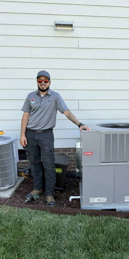 An HVAC technician standing beside a newly installed outdoor condenser unit at the side of a home