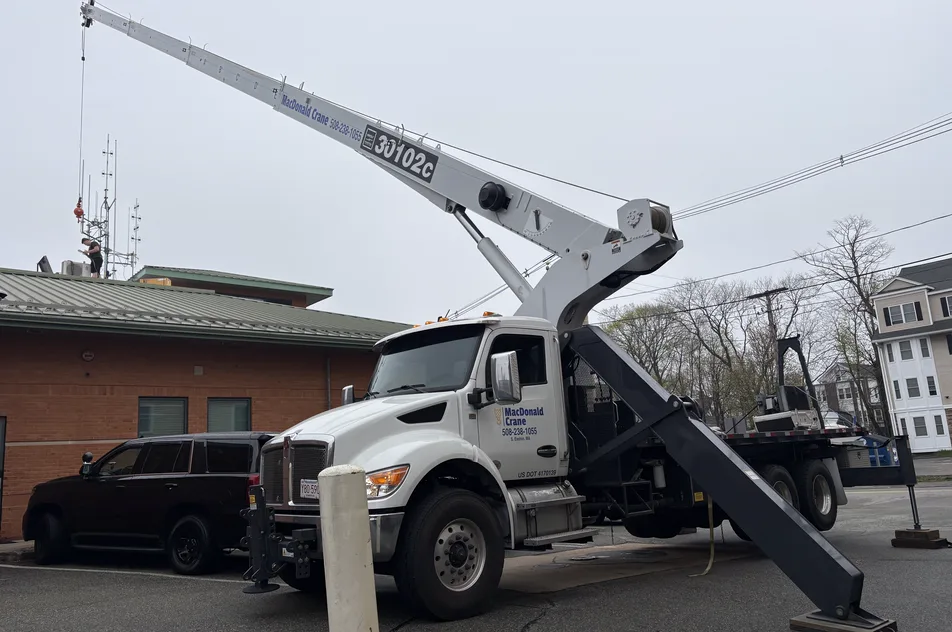 A boom truck crane set up on its outriggers at a street-side job site, boom raised.