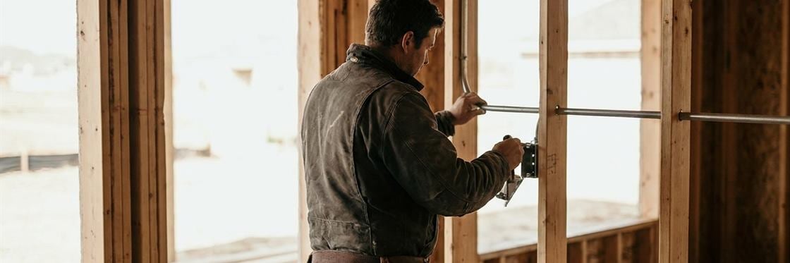 An electrician running conduit along open studs in a house under construction.