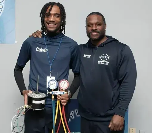 Two Su&rsquo;Coy team members standing together indoors, one holding an HVAC gauge manifold