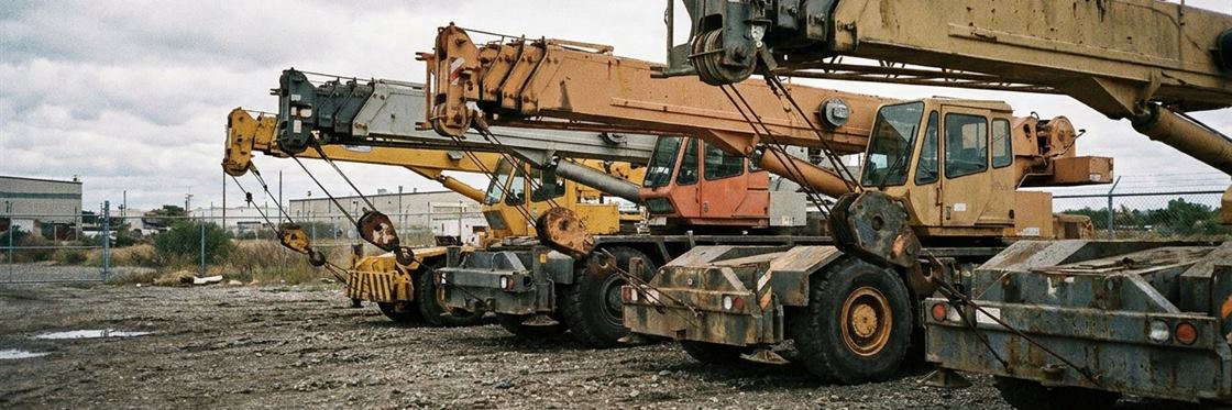 Several mobile cranes of different sizes parked with their booms stowed in a rental yard.
