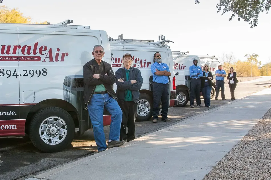 Eight members of an HVAC company standing with folded arms along a row of branded service vans.