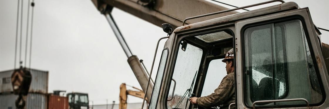 A crane operator at the controls in the cab, seen from outside the machine.
