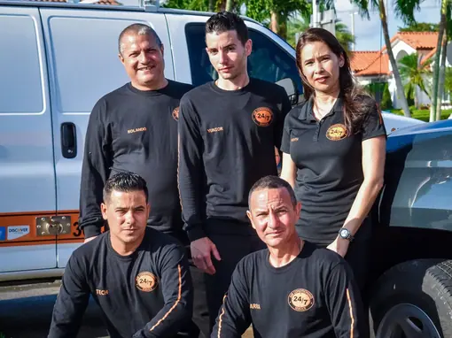 A five-person HVAC crew in branded black shirts, two kneeling in front and three standing, beside their service van
